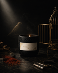 Gilded Cage black scented candle lit beside a gold birdcage and saffron in moody low light — Ironic Paradoxists