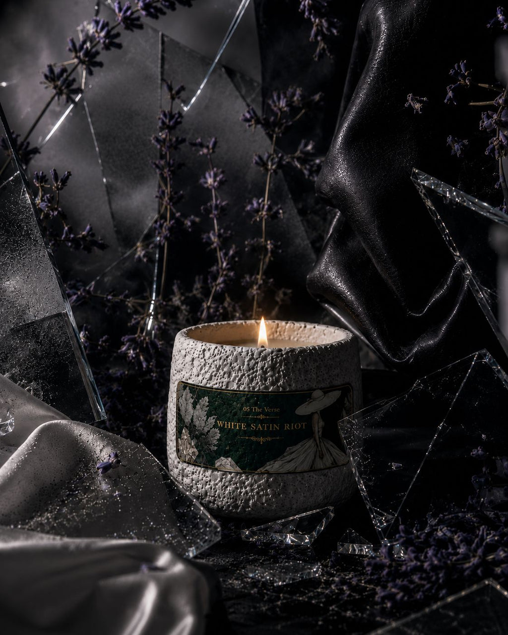 White Satin Riot candle among shattered glass, satin and lavender in dark light